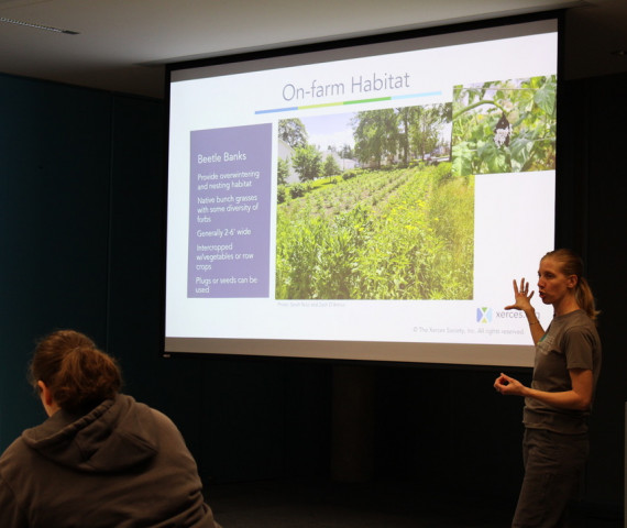 Sarah Nizzi stands in front of a screen and presents a slide about 'on-farm habitat'